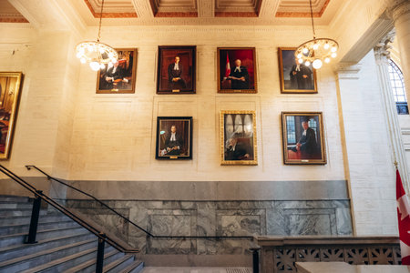 Ottawa, Canada - August 13, 2025: Interior staircase of the Senate of Canada Building with framed portraits on the wall, marble details, chandeliers, and part of a Canadian flag visible on the right.のeditorial素材