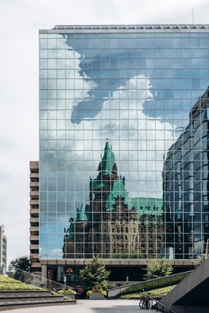 Ottawa, Canada - August 13, 2025: Reflection of the historic Confederation Building in the glass facade of a modern office tower in downtown Ottawaのeditorial素材