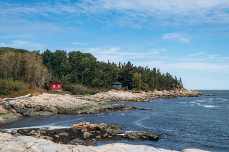 Rocky coastline with small red cabin and forest along the Saint Lawrence River in rural Quebec, Port-au-Persil, Canadaの写真素材