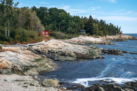 Rocky coastline with small red cabin and forest along the Saint Lawrence River in rural Quebec, Port-au-Persil, Canadaの写真素材