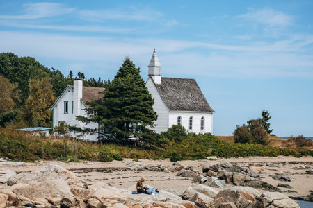 Port-au-Persil, Canada - August 20, 2025: Small white wooden chapel with bell tower overlooking the...