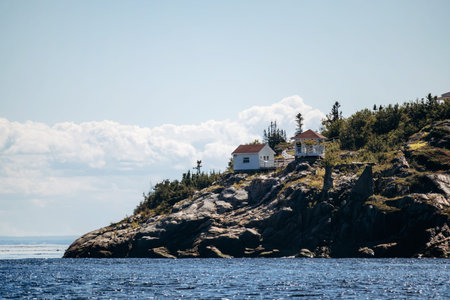 White lighthouse with red roof and assistant house on rocky cliff overlooking Saguenay-St. Lawrence Marine Park, Pointe-Noire Lighthouse, Baie-Sainte-Catherine, Quebecの写真素材
