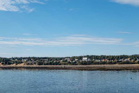 Panoramic view across Saguenay River showing Baie-Sainte-Catherine village shoreline with colorful houses and trees.の写真素材