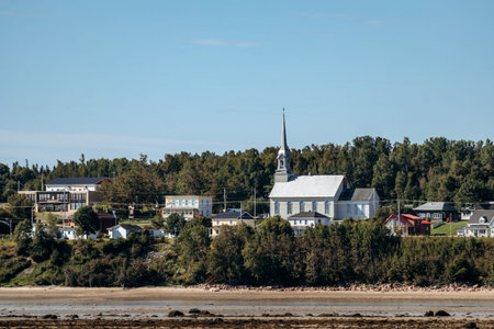 Panoramic view across Saguenay River showing Baie-Sainte-Catherine village shoreline with colorful houses and trees.の写真素材