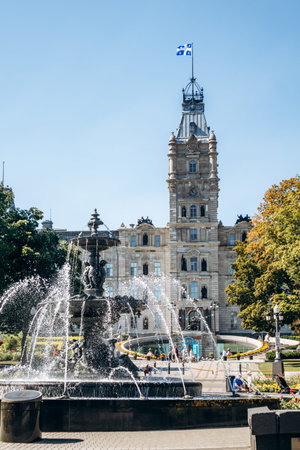 Quebec City, Canada - August 23, 2025: Fontaine de Tourny fountain with water jets in front of Quebec National Assembly building flying Quebec flag on sunny summer dayのeditorial素材