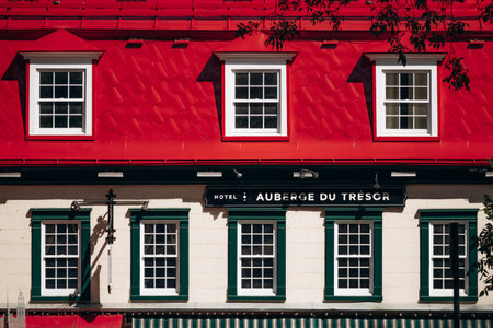 Quebec City, Canada - August 23, 2025: Hotel Auberge du Tresor facade with red roof, green shutters, outdoor terrace umbrellas and pedestrians in Old Quebec historic districtのeditorial素材