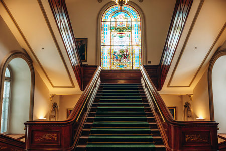 Quebec City, Canada - August 23, 2025: Grand interior staircase with green carpet and stained glass...