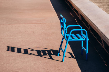 Bright blue metal chair casting a long shadow on sunlit pavement along the Croisette promenade in...