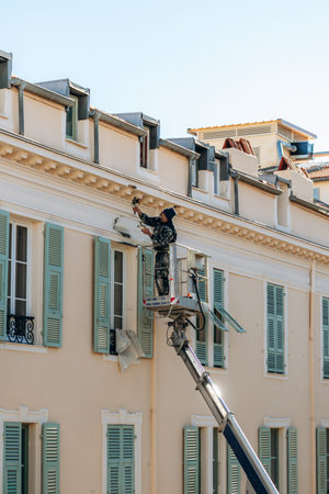 Nice, France - January 29, 2026: Worker on a lifting platform repairing the facade of a residential...