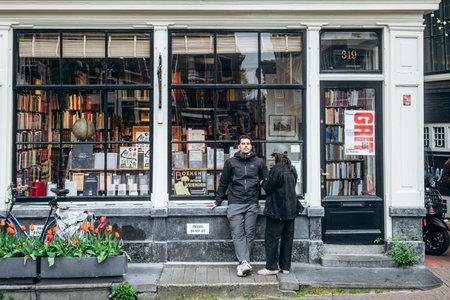 Amsterdam, Netherlands - April 18, 2026: Traditional bookstore facade with large windows and visitors on a canal-side street in Amsterdam city center