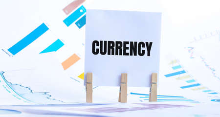 CURRENCY text on paper sheet with chart, dice, spectacles, pen, laptop and blue and yellow push pin...