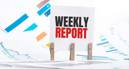WEEKLY REPORT laptop and blue and yellow push pin on wooden table - business, banking, finance and investment conceptの写真素材