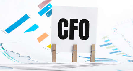 cfo text on paper sheet with chart, dice, spectacles, pen, laptop and blue and yellow push pin on wooden table - business, banking, finance and investment conceptの写真素材