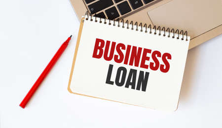 Laptop, red pen and notepad with text BUSINESS LOAN in the white backgroundの写真素材