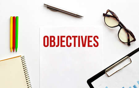 Paper plate, glasses, notepad, pen and pencils on the white background. Business concept. Text OBJECTIVESの写真素材