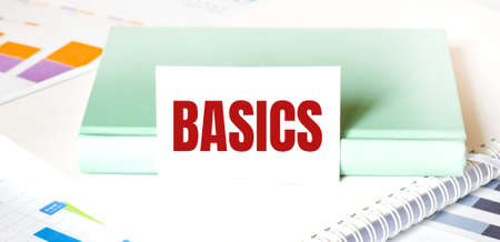 Financial diagram on white big notepad, green book and paper sheet with text BASICS. Business conceptの写真素材
