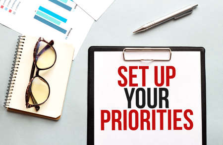 Business concept. Notebook with text Set up your priorities sheet of white paper for notes, glasses...