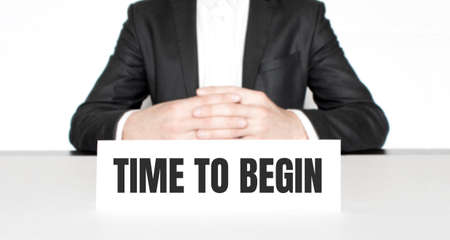 Businessman sitting at the table and signboard with text TIME TO BEGIN. Business conceptの写真素材