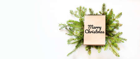 Brown notepad lying on branches of a christmas tree with text Merry Christmasの写真素材