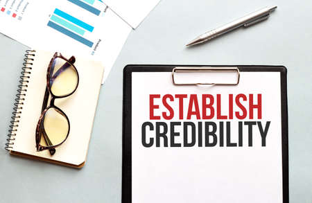 Business concept. Notebook with text ESTABLISH CREDIBILITY sheet of white paper for notes, glasses in the white backgroundの写真素材