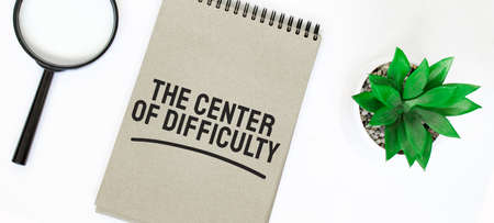 A magnifying glass, a blank brown notebook on a white table. center of difficulty sign