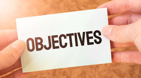 OBJECTIVES word inscription on white card paper sheet in hands of a businessman. recap concept. red and white paperの写真素材