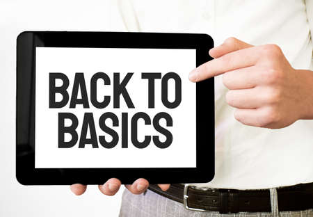 Text BACK TO BASICS on tablet display in businessman hands on the white bakcground. Business conceptの写真素材