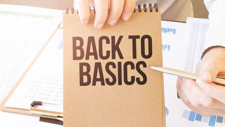 Text BACK TO BASICS on brown paper notepad in businessman hands on the table with diagram. Business conceptの写真素材
