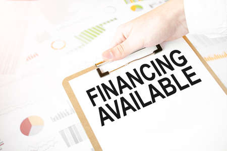 Text FINANCING AVAILABLE on white paper plate in businessman hands with financial diagram. Business conceptの写真素材