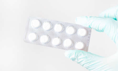 Surgeon's hand in a blue medical glove holds a blister of tablets isolated on a white