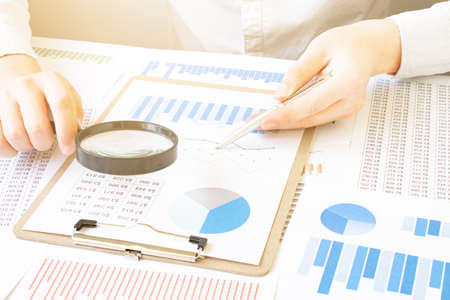 Close-up Of A Businessperson's Hand Looking At Receipts Through Magnifying Glass At Workplace