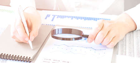Close-up Of A Businessperson's Hand Looking At Receipts Through Magnifying Glass At Workplace