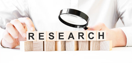 Businessman holding magnifier and wood block. Businessman watch on the wooden cubes with text RESEACRH. financial market. financingの写真素材