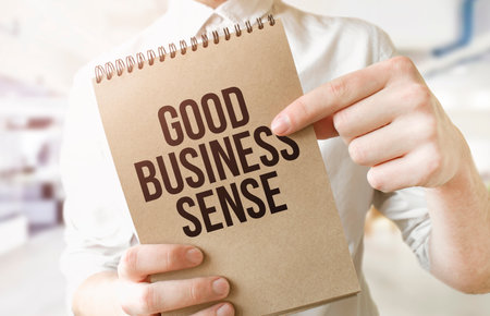 Text GOOD BUSINESS SENSE on brown paper notepad in businessman hands in office. Business conceptの写真素材