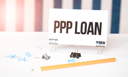 PPP LOAN sign on paper on white desk with office tools. Blue and white backgroundの写真素材