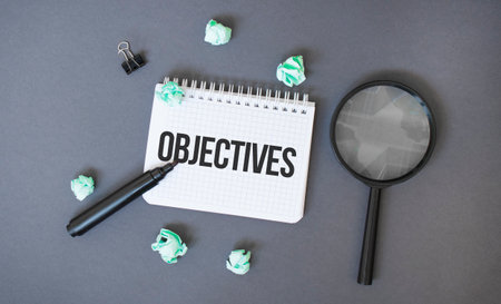 Paper notepad with text OBJECTIVES, crumpled papers sheets and magnifier glass on dark backgroundの写真素材