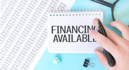 Businesman hand with marker and white noteapad and magnifier on the financial documentation. Text FINANCING AVAILABLE. Business conceptの写真素材