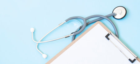 A wooden clipboard and stethoscope with white paper on it, set against a blue backgroundの写真素材