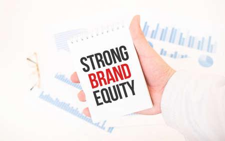 Businessman holding a white notepad with text STRONG BRAND EQUITY, business conceptの写真素材