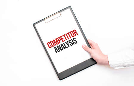 A businessman holds a folder with paper sheet with the text COMPETITOR ANALYSIS. Business concept.の写真素材