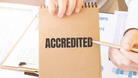 Text Accredited on brown paper notepad in businessman hands on the table with diagram. Business conceptの写真素材
