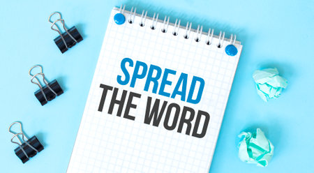 White notepad with text Spread the word and office tools on the blue backgroundの写真素材