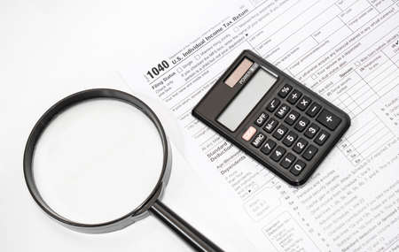 Tax form 1040, magnifiying glass and calculator in office workplace. Business concept.