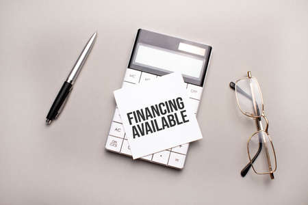 pen, calculator and glasses on gray background. Business concept. White paper sheet with FINANCING AVAILABLE signの写真素材