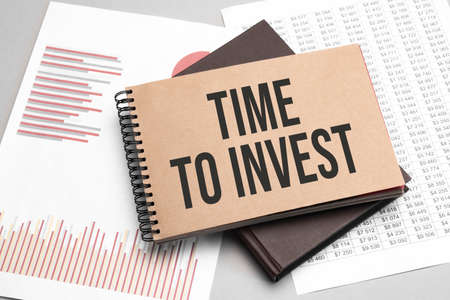 Notepad with text TIME TO INVEST on a white background, near laptop, calculator and office supplies....