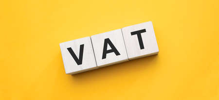 Vat on wooden cubes over yellow background, financial concept background