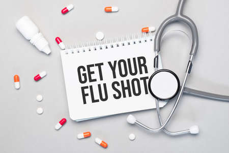 In the notebook is the text GET YOUR FLU SHOT, next to a stethoscope, pills and glasses.の写真素材