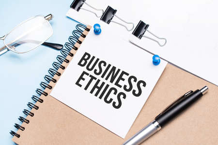 Notepad with BUSINESS ETHICS text on the office table with glasses, notepad and paper with clips.の写真素材