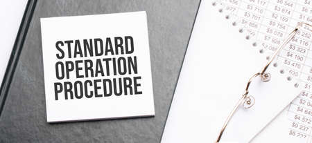 Text Standard Operation Procedure on notepad with office tools, pen on financial report. Business...