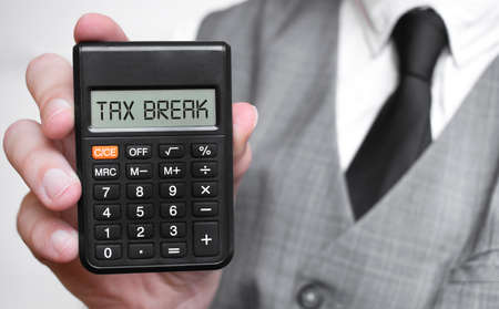 tax break word text inscription on calculator in a male hand of a businessman in white shirt and blue tie, Concept of finance and banking. close up, banner.の写真素材